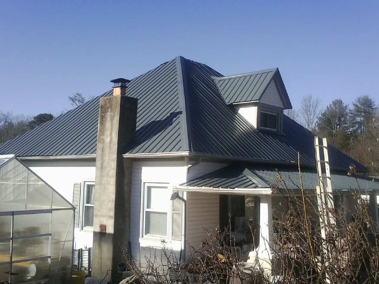 Dark blue standing seam metal roof on a white farmhouse with dormer — Slate & Tile Roof Repair by Roofing Brothers in Gilby
