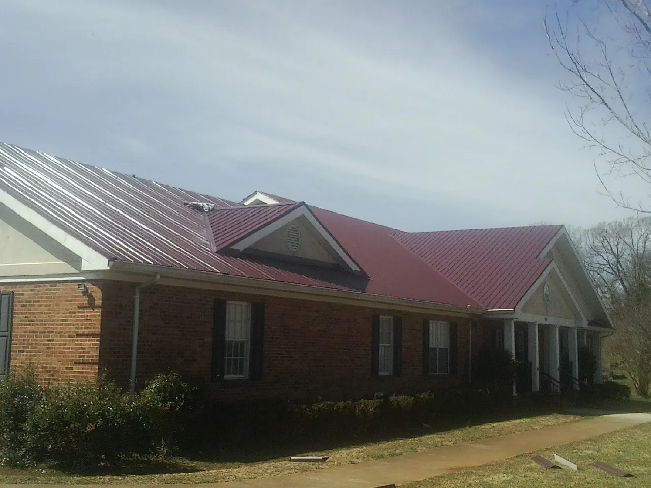 Red metal roof with gabled entries on a long brick building, from a Hail Damage Roof Repair job in Gilby