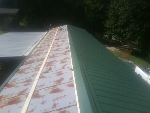 Old rusted panels beside newly installed green metal roofing — Wind Damage Roof Repair by Roofing Brothers in Gilby
