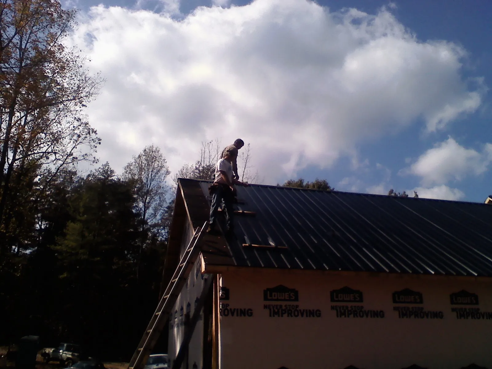Roofer fastening dark metal panels high against a cloudy sky, from a Roof Inspection job in Gilby