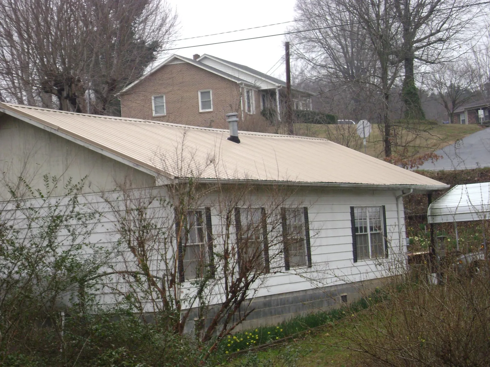 Tan metal roof on a white sided house set into a hillside — Commercial Roofing by Roofing Brothers in Gilby