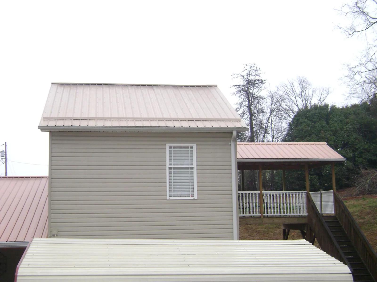Tan metal roofs on a two story addition and attached porch, from a Roof Replacement job in Gilby